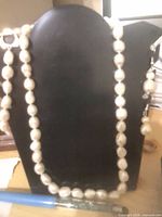 Full view of white pearl necklace on black display form