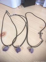 Three black cord necklaces each with rough purple stone pendants and extender chains