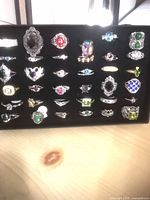 Front view of black case holding four rows of assorted plated rings on velvet insert