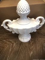 Front view of white ceramic lidded urn showing handles and pedestal base