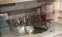 Countertop view of plastic containers, glassware, ceramic serve pieces, measuring cup, green tray and glass vases