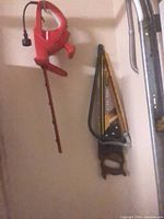 Red corded electric saw hanging beside two manual hand saws