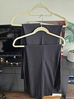 Two pairs of black/charcoal dress pants folded over hangers front view