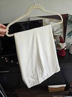 Full view of folded ivory dress pants on hanger showing overall color and fabric