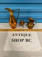 Group shot of copper pitcher, creamer and burner beside ruler