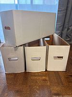 Four white comic long boxes, three upright side-by-side, one resting on top, showing front carry handle slots and overall condition