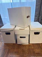 Four white short comic boxes stacked, showing three lids and one lidless