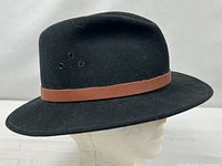 Left profile of black wool felt hat on mannequin showing brown leather band and ventilation holes