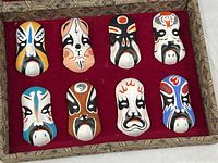 open box showing eight painted masks mounted on red fabric