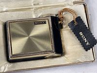 Front view of Sony TR-81 in case showing gold grille, SONY badge, cord, hangtag