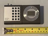 Front view showing speaker grid, LCD display, control buttons and scale reference