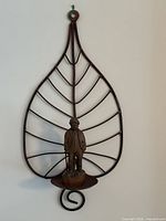 Full view of wrought metal leaf-shape wall frame with wooden figure on platform