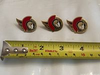 Front view of three Ottawa Senators pins with measuring tape showing size