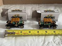 Both Model T cars alongside tape measure showing length with boxes behind