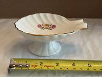 Top angle showing shell-shaped bowl, floral motif and length against tape measure