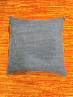 Front view of blue square pillow on orange background