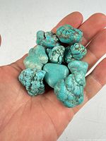 Hand holding nine rough turquoise stones