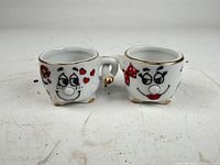 front view of both anthropomorphic cups showing painted faces, gold rims and handles