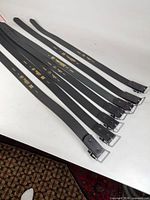 Seven black Boston Leather belts laid out showing overall condition and buckles