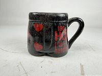 Front view showing text "too HOT to handle!" on black ceramic mug shaped like shorts.
