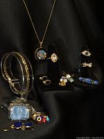 Full group view of jewelry on black fabric, showing necklace, bracelets, rings, brooch and earrings