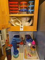 Cabinet and countertop view showing storage containers, mixing bowls, drink bottles and straws