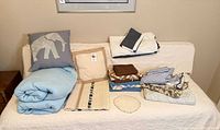 Full lot on sofa showing pillow, blue blanket, crochet throw, doily and stacked linens