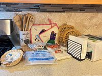 Full lot on countertop showing utensils in crock, potholders, trivets, gloves, paper goods