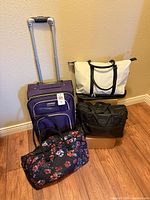 Group shot of four bags: purple rolling suitcase, cream tote, black briefcase, floral quilted duffel