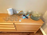 Overall lot on sideboard showing glass bowls, mugs, utensils, wire basket