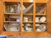 Cabinet view showing entire mixed lot of bakeware, plates, storage jars and containers