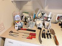 Overall lot on countertop showing hand tools, garden tools, hardware bins and gloves