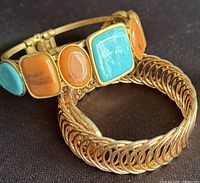 Close view of two bracelets: hinged cuff with cabochon stones and gold-tone stretch loop bracelet