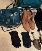Overview of teal leather handbag, two pairs suede boots, two pairs gloves, wooden shoe trees on carpet