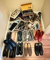 Floor grouping of multiple shoe pairs including red and black ankle boots, clogs, loafers and several boxed pairs