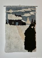 Full view of hand-hooked wool wall hanging showing winter cabin scene, hanging rod visible
