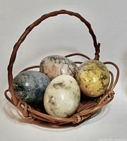 four polished stone eggs in wicker basket