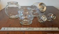 Group shot of four glass jars with ruler for scale, showing lids and bear jar