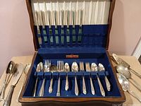 Open wooden chest showing majority of flatware pieces arranged in slots