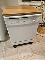 Front view of white GE portable dishwasher showing control panel, laminate top and casters