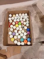Open box showing rows of white and colored golf balls with tees