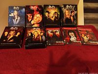Buffy seasons 1-7 and three Hellsing DVDs displayed on red surface