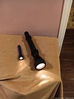 Large black and small blue Mag-Lite flashlights lit on towel