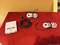 Console, two controllers, HDMI and power cable laid out on red surface