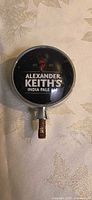 Front view of round Alexander Keith's tap badge showing logo and condition