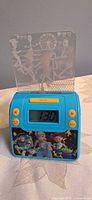 Front view showing blue casing, yellow buttons, digital display, Toy Story decal, clear etched projection plate