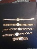 All five gold-tone wristwatches on black background