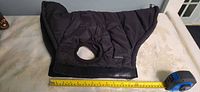 OnePaw black quilted dog coat folded, showing harness hole and Velcro belly strap with tape measure for scale