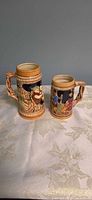 Front view of both ceramic beer steins showing scenic designs