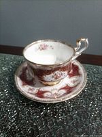 Teacup on saucer showing burgundy and gold design